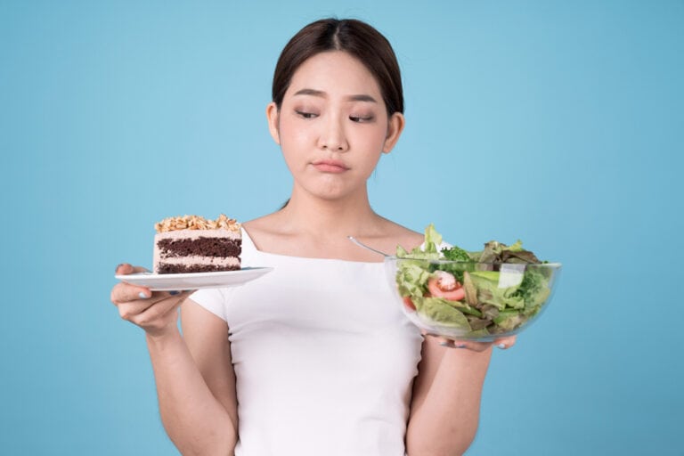 ผู้หญิงชั่งใจระหว่างสลัดเพื่อสุขภาพและเค้ก ซึ่งเป็นอาหารที่ทำให้ตับทำงานหนัก